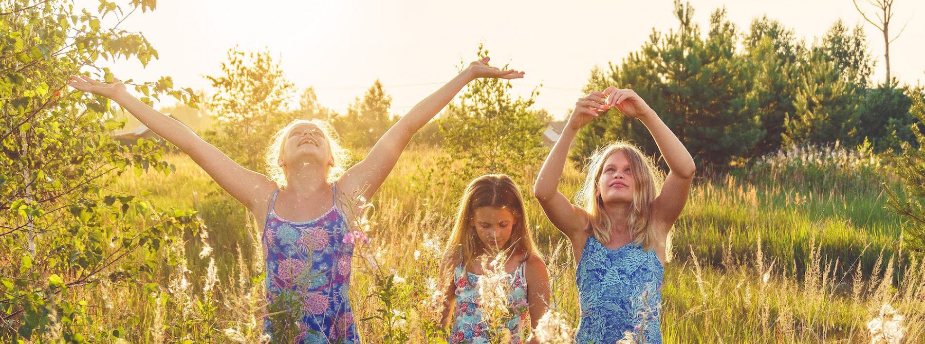 drei Mädchen stehen auf einer Wiese inmitten von Gras und Blumen